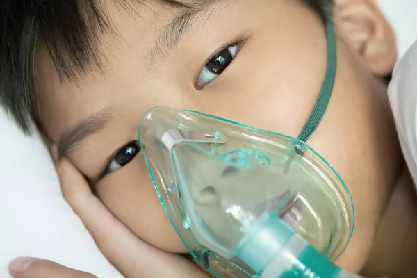 Close up sick Yong asian boy with face oxygen mask lay on a white bed at hospital. COVID 19 concept.