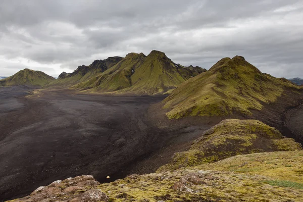 Меланхоличные пейзажи Исландии с бесконечной черной лавовой пустыней и зелеными горами, покрытыми толстыми — стоковое фото