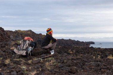 Snaefellsness İzlanda Jul 23 2016 Volkanik siyah lav üzerinde oturan büyük sırt çantası ile genç kadın