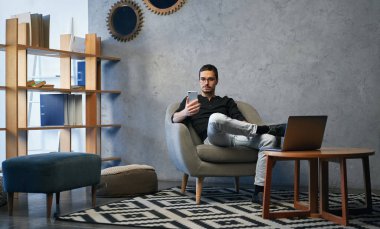 Genç adam telefon ve bilgisayarla çalışıyor, telefon alıyor, ortaklarla konuşuyor. 