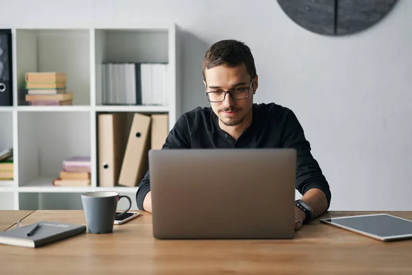 Young man working with computer, phone and tablet at the table while drinking coffee — Stock Photo, Image