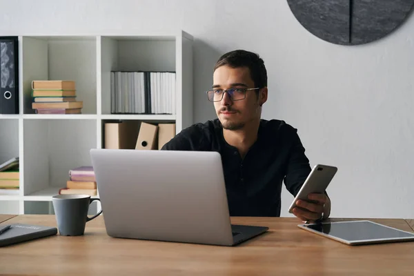 Joven trabajando con el teléfono y la computadora, recibiendo llamadas telefónicas, hablando con los socios — Foto de Stock