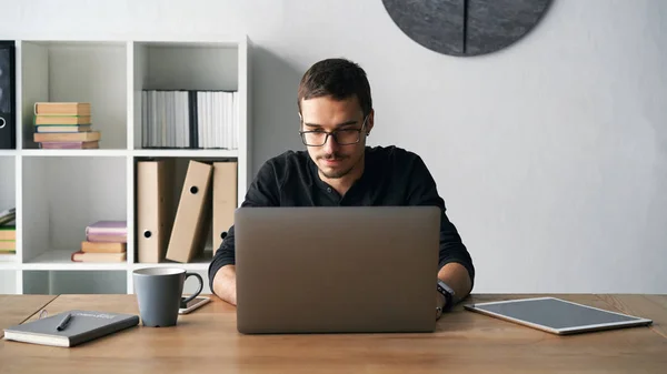 Giovane che lavora con computer, telefono e tablet a tavola mentre beve caffè — Foto Stock