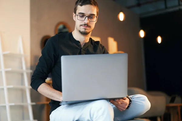 Joven sentado con la computadora. Freelancer en gafas trabajando con laptop, project manager . — Foto de Stock