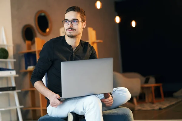 Joven sentado con la computadora. Freelancer en gafas trabajando con laptop, project manager . — Foto de Stock