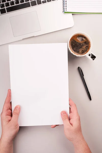 Mans hands holding blank paper on the working desk with computer and coffee — Stock Photo, Image