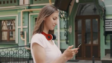Telefonda doğru yolu arayan genç bir kadın. Kırmızı kulaklık takıyor ve beyaz t-shirt takıyor.