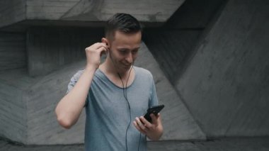 Genç gülen adam kulaklığı kulağına yerleştirir. Dışarıdaki video görüşmesinden önce.