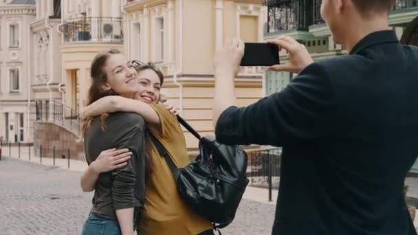 Dos chicas hermosas jóvenes fotografiadas por el hombre en el teléfono inteligente. Concéntrate en el teléfono al final . — Vídeos de Stock