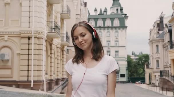 Joven mujer feliz caminando y escuchando música desde el teléfono con auriculares rojos — Vídeos de Stock