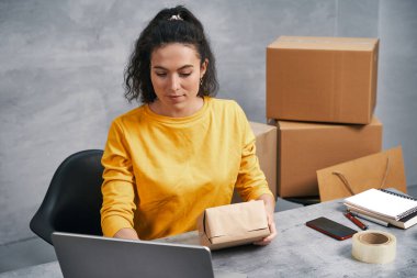 Kadın, dizüstü bilgisayarını kullanarak paket gönderiyor. Evden çalışmak