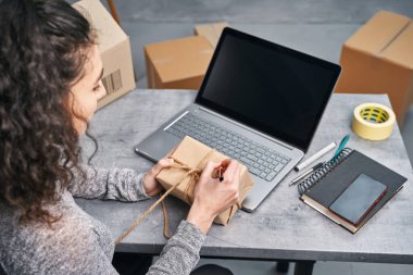 Kadın, dizüstü bilgisayarını kullanarak paket gönderiyor. Evden çalışmak