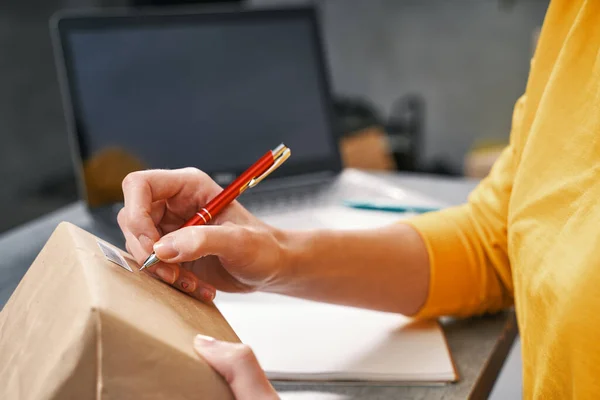 Donna che scrive l'indirizzo sul pacco. Lavorare da casa in quarantena — Foto Stock