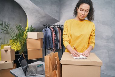 Kadın evden çalışıyor, paket gönderiyor, paketin üzerine adres yazıyor.