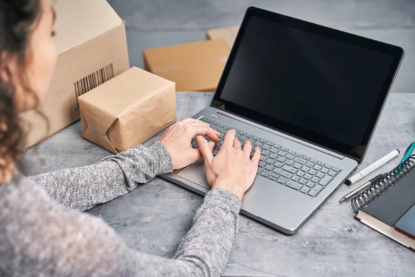 Una donna che manda pacchi usando il suo portatile. Lavorare da casa Foto Stock