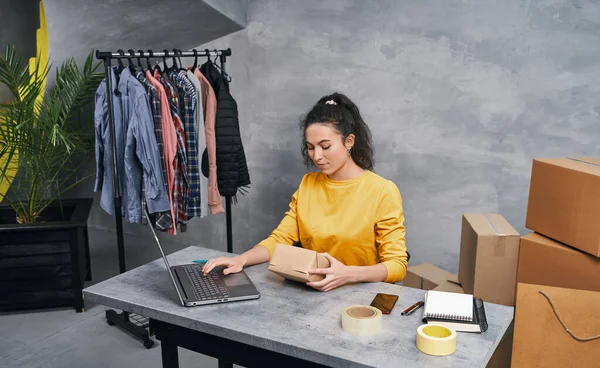 Una donna che manda pacchi usando il suo portatile. Lavorare da casa Foto Stock