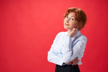 Kırmızı arka planda poz veren güzel kızıl saçlı kadın.