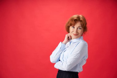 Kırmızı arka planda poz veren güzel kızıl saçlı kadın.