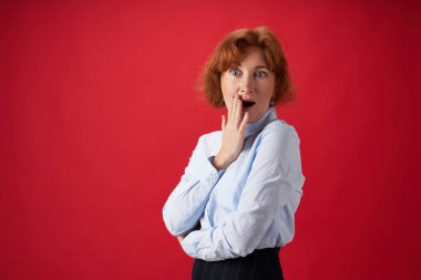 Güzel kızıl saçlı kadın kırmızı arka planda şaşırdı.