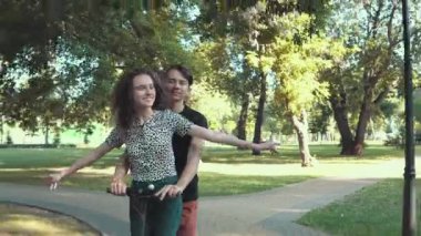 Elektrikli scooter kullanan ve elleriyle titanik pozlar veren genç bir çift.