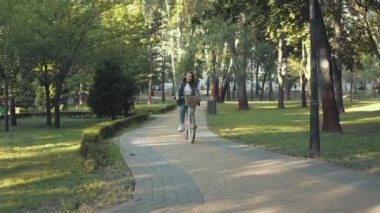 Güneşli bir sabahta parkta bisiklet süren mutlu bir kadın.