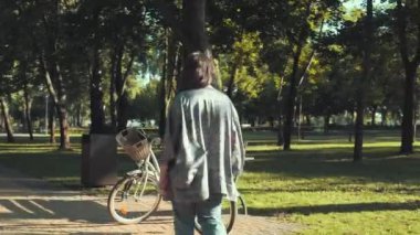 Kadın güneşli bir günde bisikletle parka gidiyor.