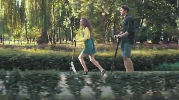 Pareja joven montando scooters en el parque — Vídeos de Stock