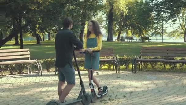 Nastolatki rozmawiające w parku podczas jazdy na skuterach elektrycznych — Wideo stockowe