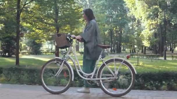 Mulher andando com sua bicicleta no parque na manhã ensolarada — Vídeo de Stock