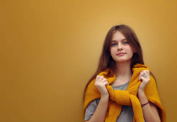blue eyed brown haired shy girl with flowing hair in a sweater on a brown background