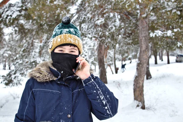 talking on the phone boy in a knitted hat with a bubo and balaclava on a winter walk