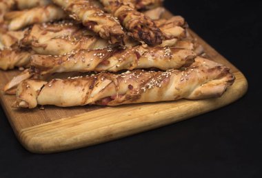 siyah zemin ahşap bir gemide jambon ve susam tohumu ile bükülmüş peynir ekmek sopa