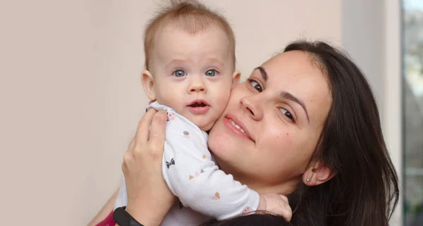 Joven madre sostiene a su divertido, dulce bebé en sus brazos —  Fotos de Stock