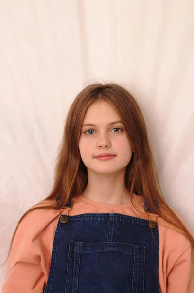 Blue eyed brown haired shy girl in denim overalls. Studio model shot. — Stock Photo, Image