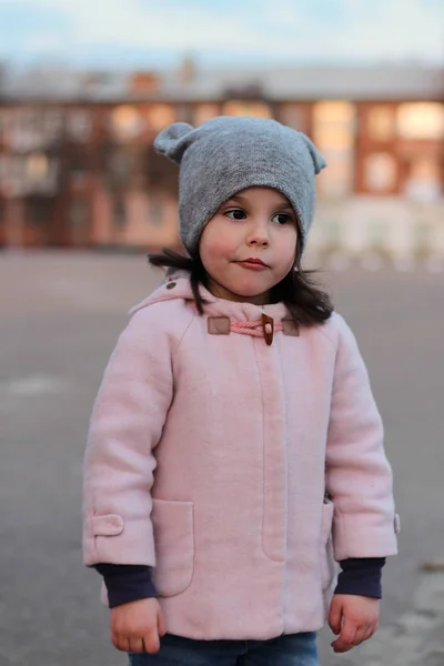 Sértett kis fehér lány sétál az utcán este. Portré a háttérben a naplemente városkép — Stock Fotó