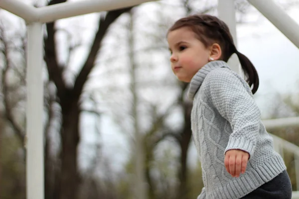 Little girl with pigtails in a sweater plays at the construction site — Stock Photo, Image