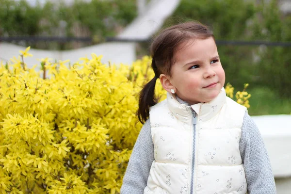 Usmívající se holčička s ponockami na pozadí keře se žlutými květy — Stock fotografie