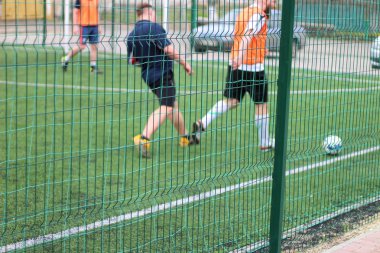 Bölüm yeşil çit odaklı görüntü. Bir top ile futbolcular arka planda oynar.