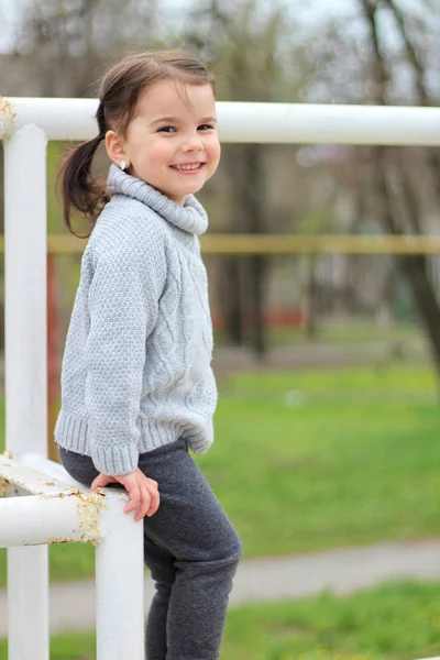 Beetje vrolijk brunette meisje in een trui en met staarten staat op een metalen structuur op bouwplaats — Stockfoto