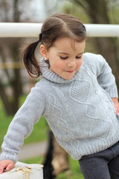 Beetje vrolijk brunette meisje in een trui en met staarten staat op een metalen structuur op bouwplaats — Stockfoto