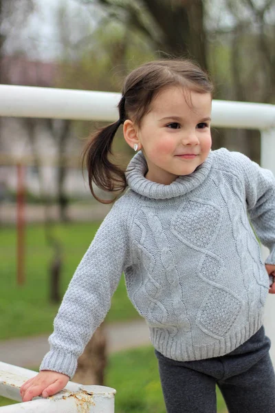 Malá veselá brunetka v svetru a s ocasy stojí na kovové konstrukci na staveništi — Stock fotografie