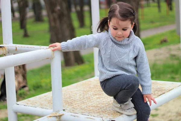 Kleines fröhliches brünettes Mädchen im Pullover und mit Frack steigt auf einer Baustelle auf eine Metallkonstruktion herab — Stockfoto