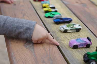 küçük bir çocuk el ahşap kırmızı-sarı masa üzerinde araba çok sayıda arasında bir oyuncak araba işaret