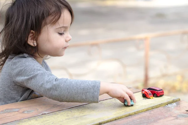 Uma mão de crianças pequenas aponta para um carro de brinquedo entre uma infinidade de carros em uma mesa de madeira vermelho-amarela — Fotografia de Stock
