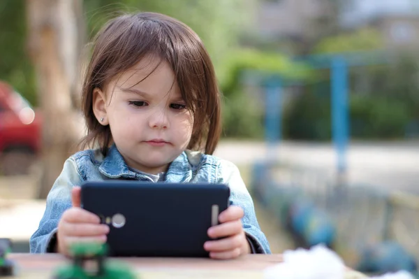 bir kot ceket kız elinde tutar ve oyun alanında bir masada otururken akıllı telefon içine bakar