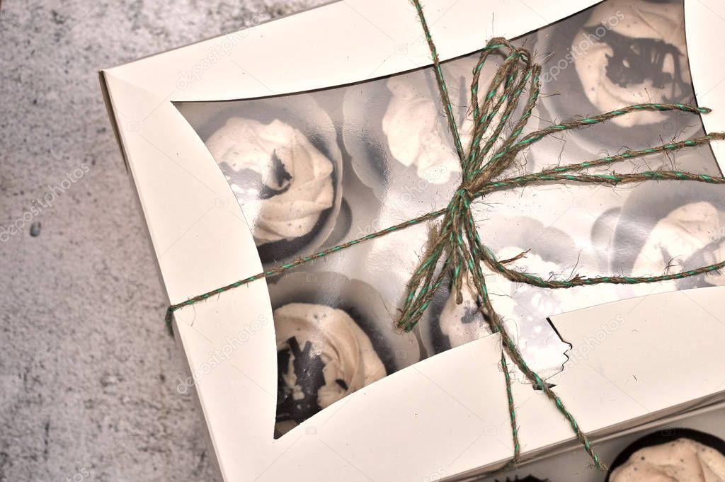 beautiful chocolate cakes covered with cream in a white box tied with a rope on a concrete background