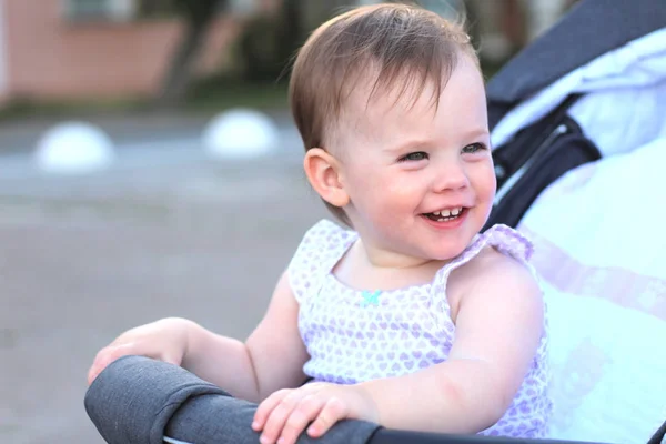 Pequeno, bonito, sorrindo, bebê ruiva bonito em um carrinho fora de portas em uma camisa sem mangas — Fotografia de Stock