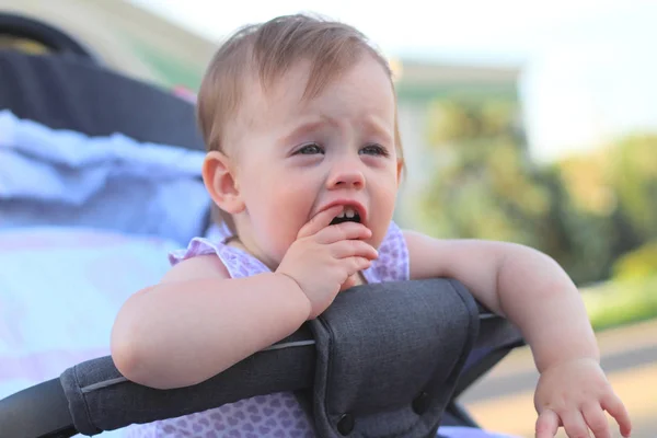 Pequeno, bonito, sorrindo, bebê ruiva bonito em um carrinho fora de portas em uma camisa sem mangas segurando os dedos em sua boca — Fotografia de Stock