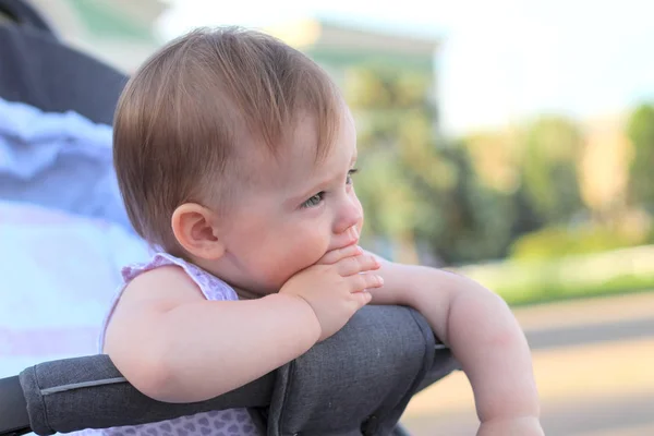 Weinig, mooi, glimlachend, schattige roodharige baby in een kinderwagen out-of-Doors in een mouwloos shirt met vingers in zijn mond — Stockfoto