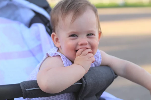 Pequeño, hermoso, sonriente, lindo bebé pelirrojo en un cochecito al aire libre en una camisa sin mangas sosteniendo los dedos en su boca —  Fotos de Stock